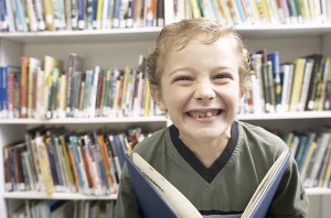 smiling-little-boy-holding-book-in-library-uid